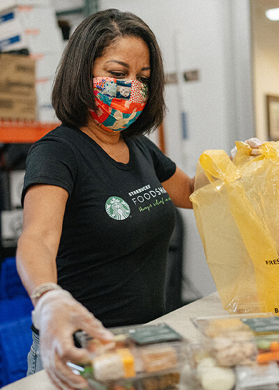 Woman wearing a Starbucks FoodShare shirt volunteering in a food bank.