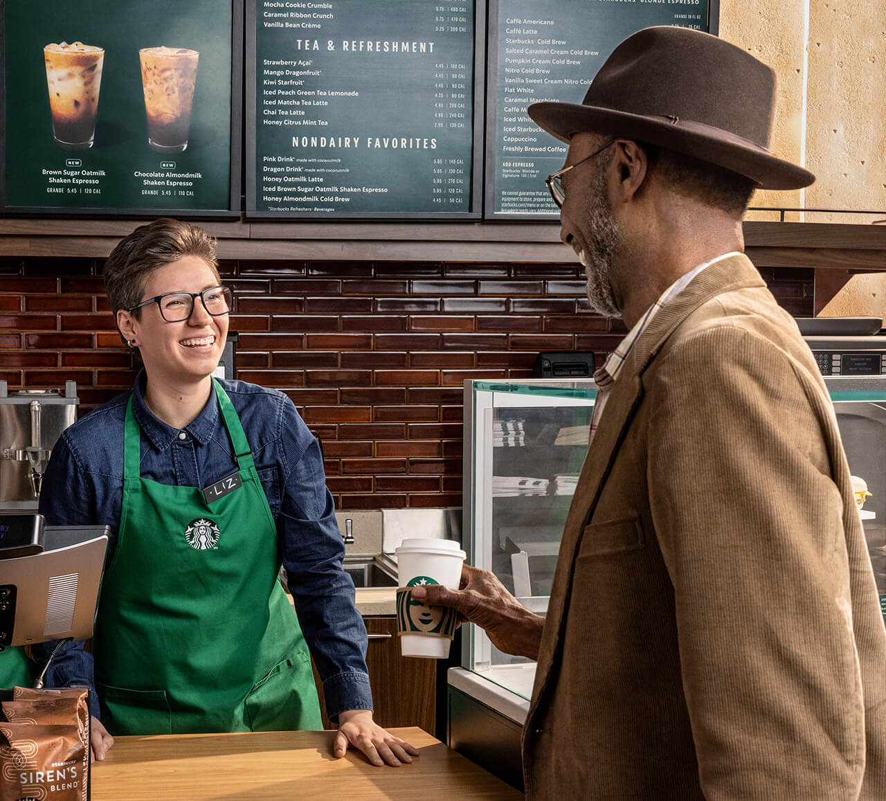 A smiling barista serves a Starbucks hot coffee to an older customer.