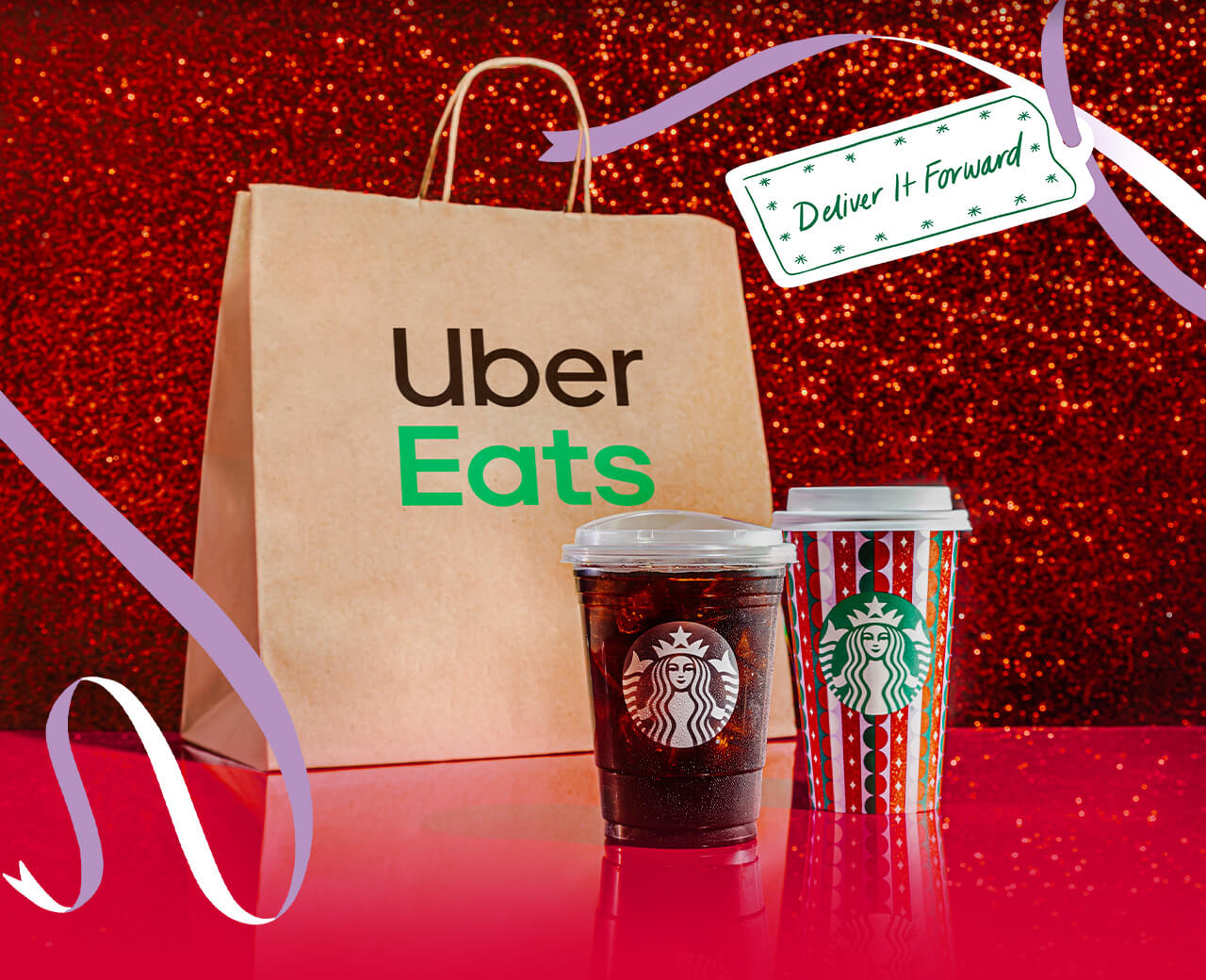 An iced coffee and a holiday hot beverage cup in front of an Uber Eats bag. Illustrated ribbons and a gift tag with "Deliver it forward" surround the bag and beverages.