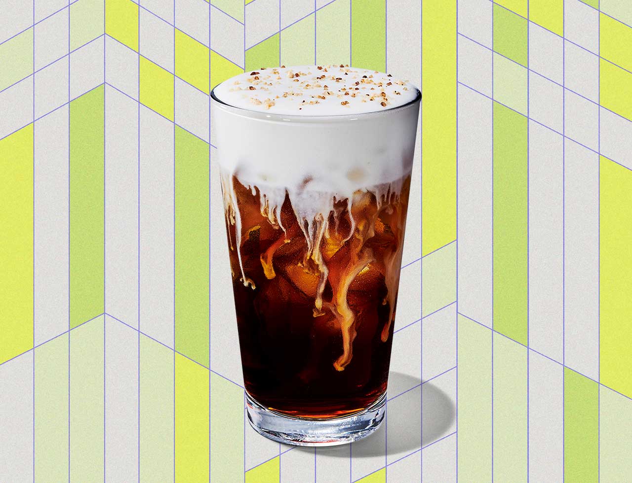 A coffee drink with a thick, foamy topping in a tall glass in front of a geometric background.