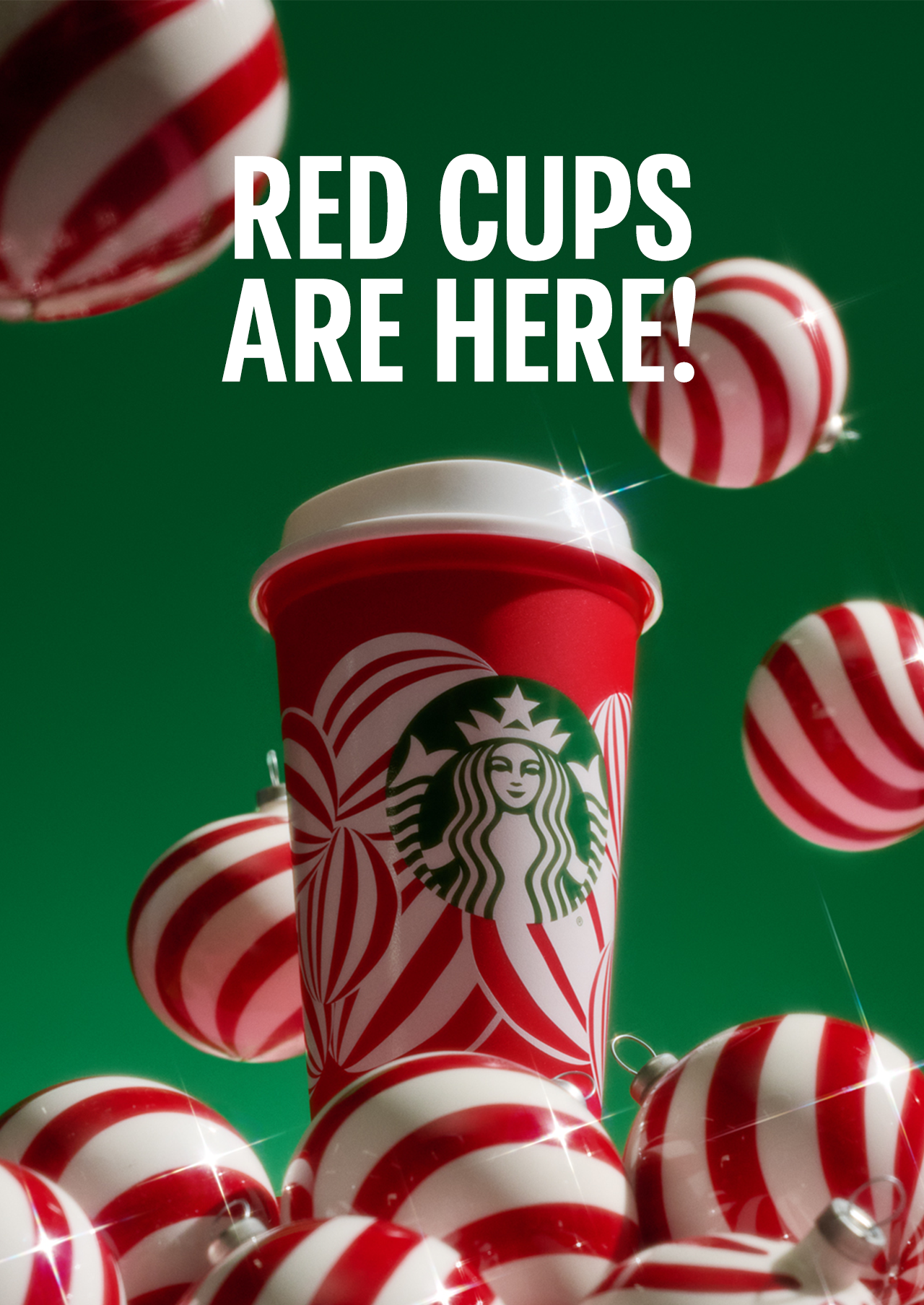 RED CUPS ARE HERE! | A Starbucks Reusable Red Cup on a pile of red and white holiday ornaments.