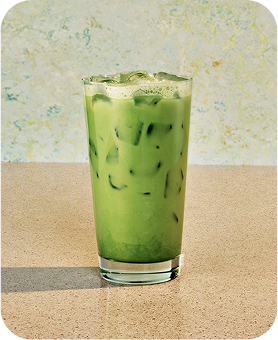 An Iced Matcha Latte sitting on a tabletop with a sage green backdrop.