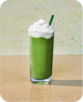 A Matcha Crème Frappuccino Blended Beverage sitting on a tabletop with a sage green backdrop.