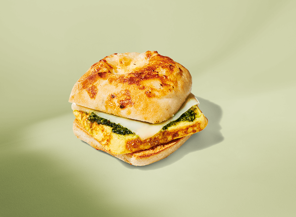 A light, fluffy, egg sandwich with melted cheese and pesto on a small plate, set on a light green background.