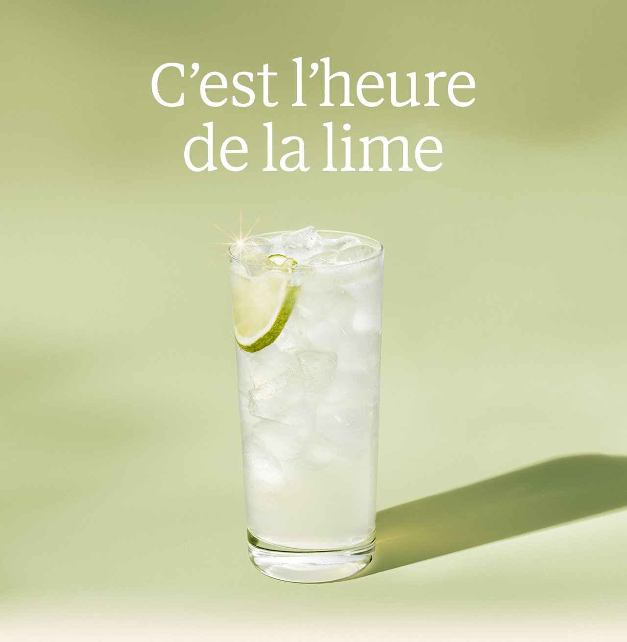 C’est l’heure de la lime | Une boisson glacée d’un vert doux brumeux capte la lumière du fond vert pâle. Une tranche de citron vert est suspendue dans la glace.