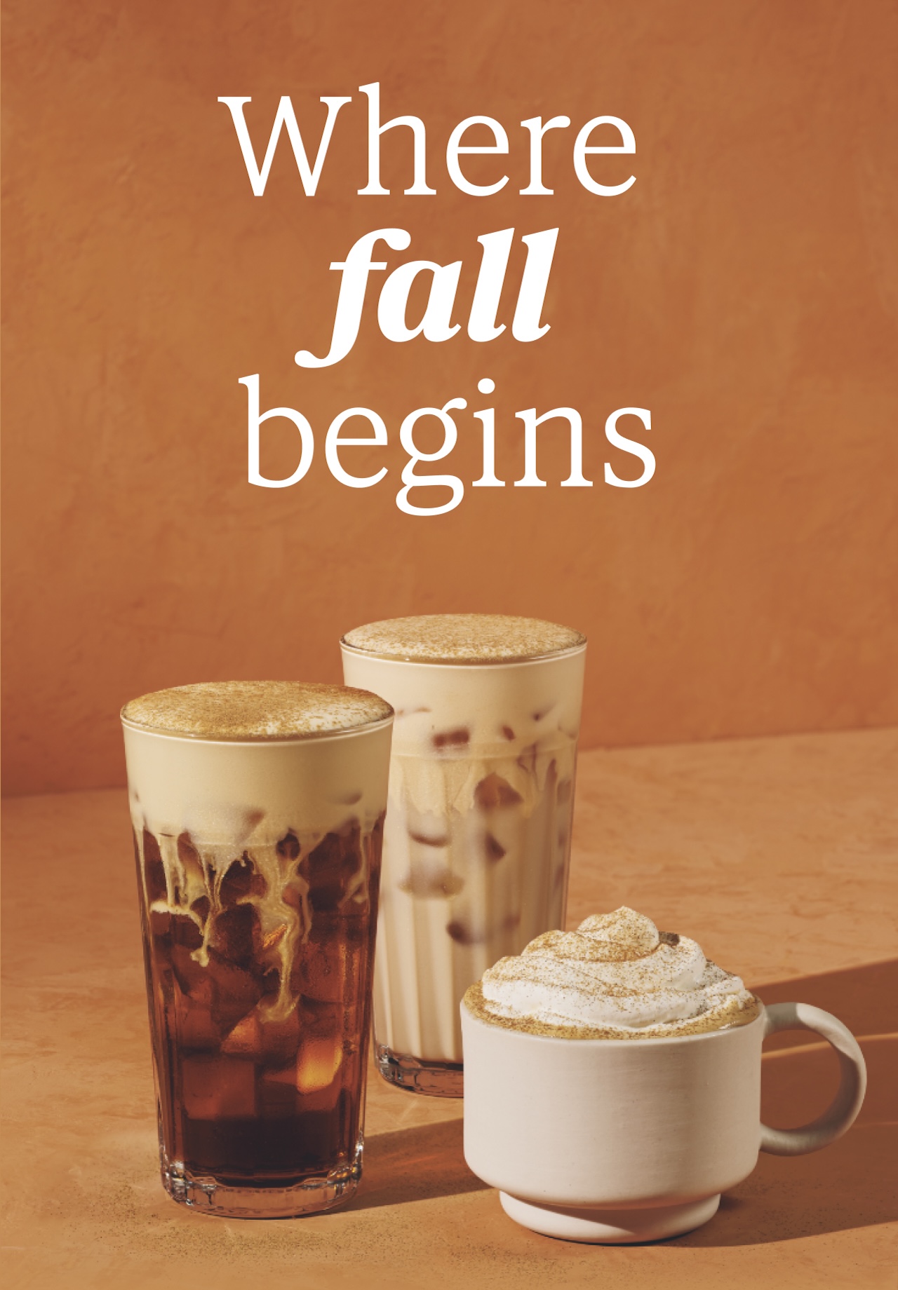 Where fall begins | Three fall beverages sit against a warm orange background. On the left, a deep brown iced pumpkin cream cold brew in a clear glass is layered with light beige cold foam and swirls of creamy white milk. In the center is a rich and creamy iced pumpkin cream chai, beige in colour and topped with delicious foam, sprinkled with pumpkin pie spices. On the right, a warm pumpkin spice latte in a white mug is crowned with delicious whipped cream and pumpkin pie spices.
