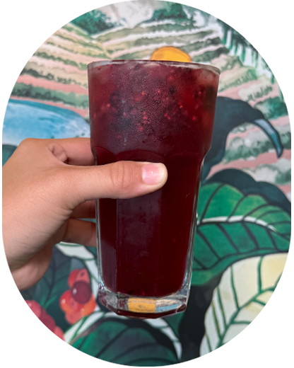 A hand holds up a Blackberry Tea Lemonade in a glass, in front of a wall painted with lush foliage.